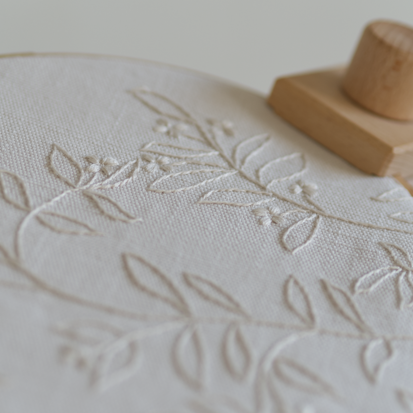 Close-up of The Branch embroidery showing detailed cream thread stitches of leaves and small flowers