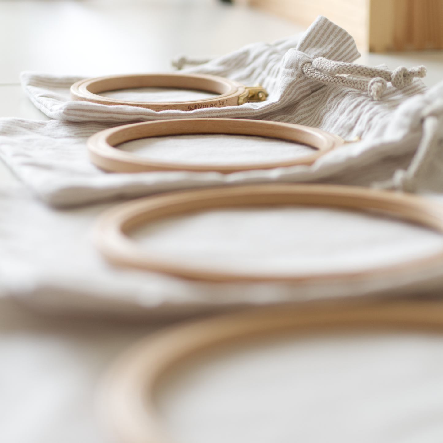 Set of four drawstring bags in different sizes laid out flat with a corresponding embroidery hoop on top of each, ready to embroider.