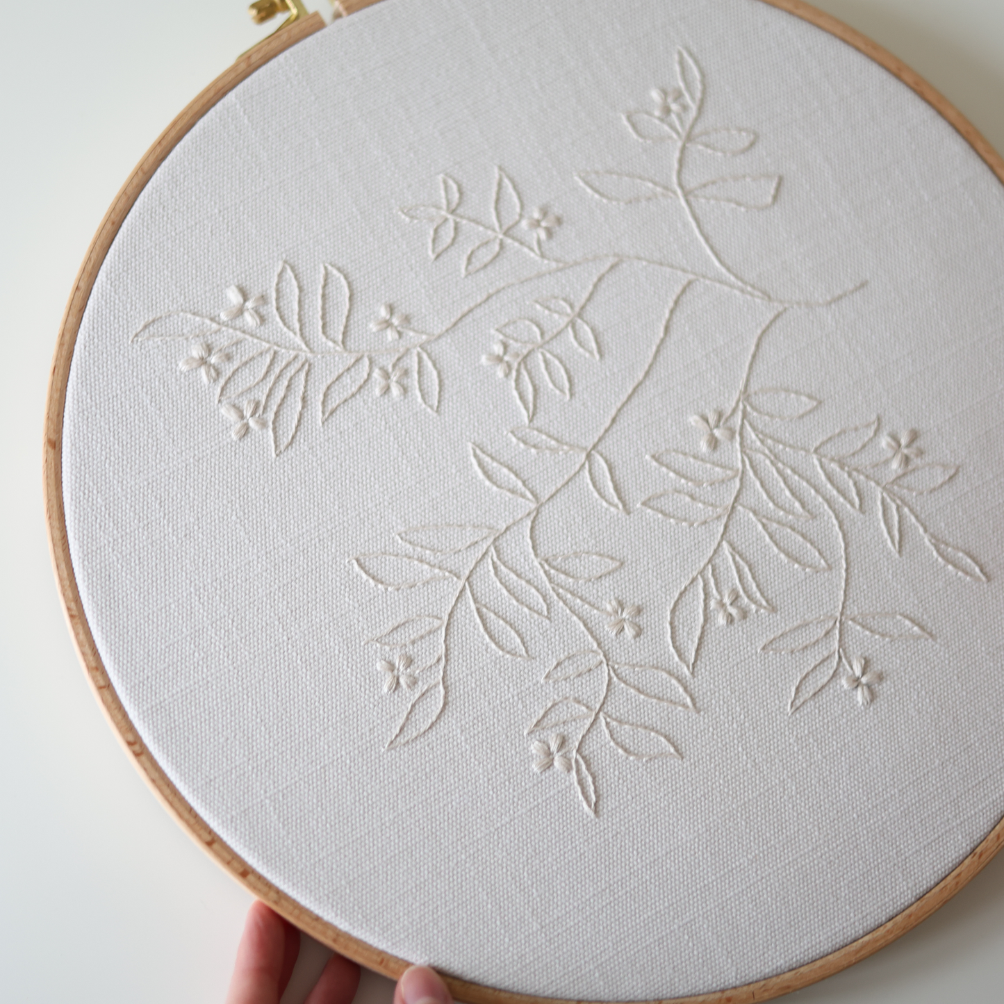 The Branch cream thread embroidery shown in wooden hoop
