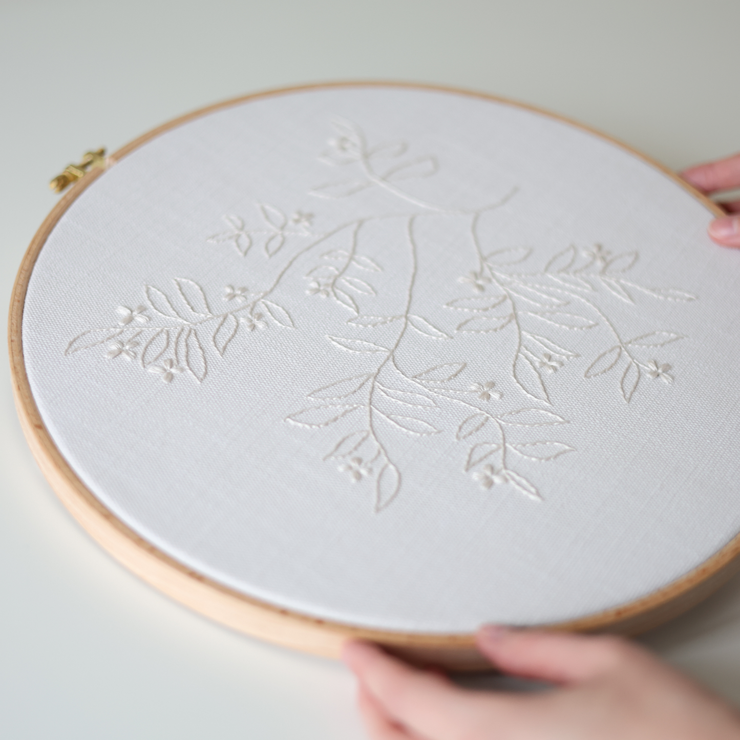 The Branch botanical embroidery displayed in a wooden hoop showing cream thread and fabric
