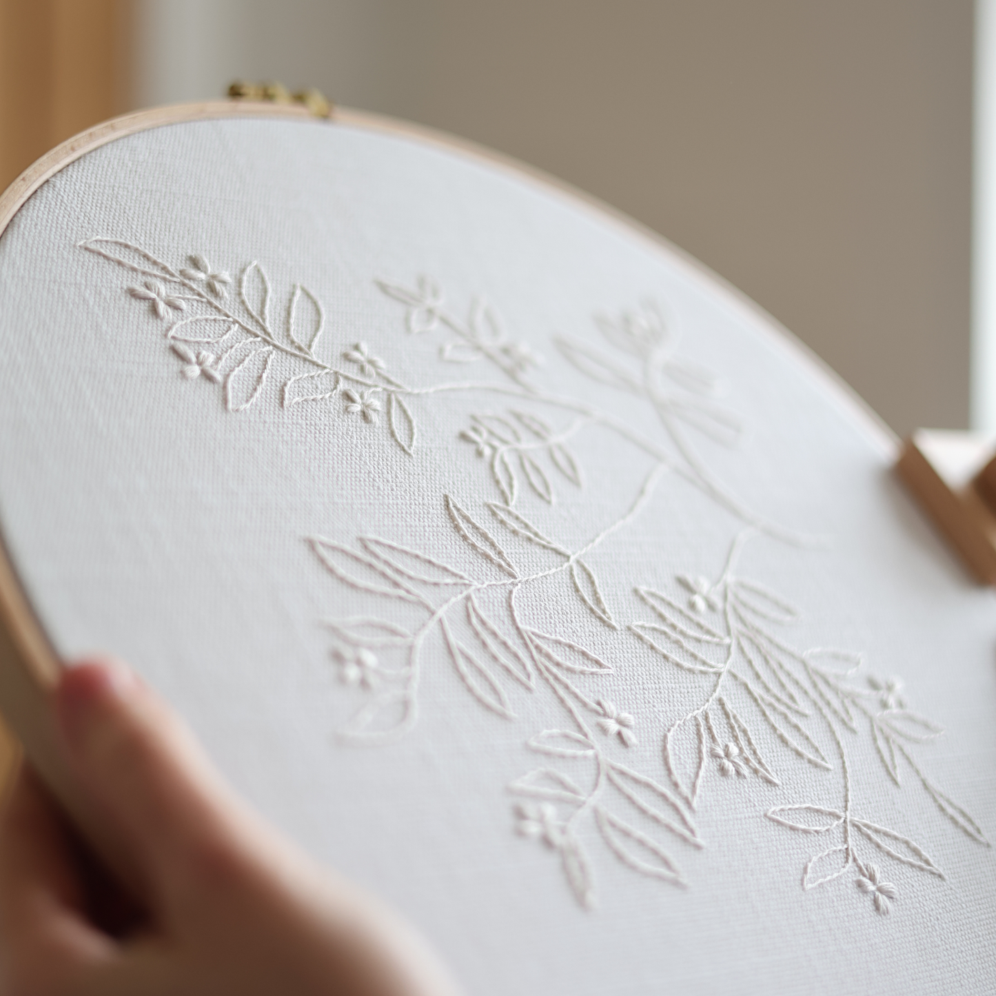 Close-up side angle of The Branch embroidery showing detailed cream thread stitches