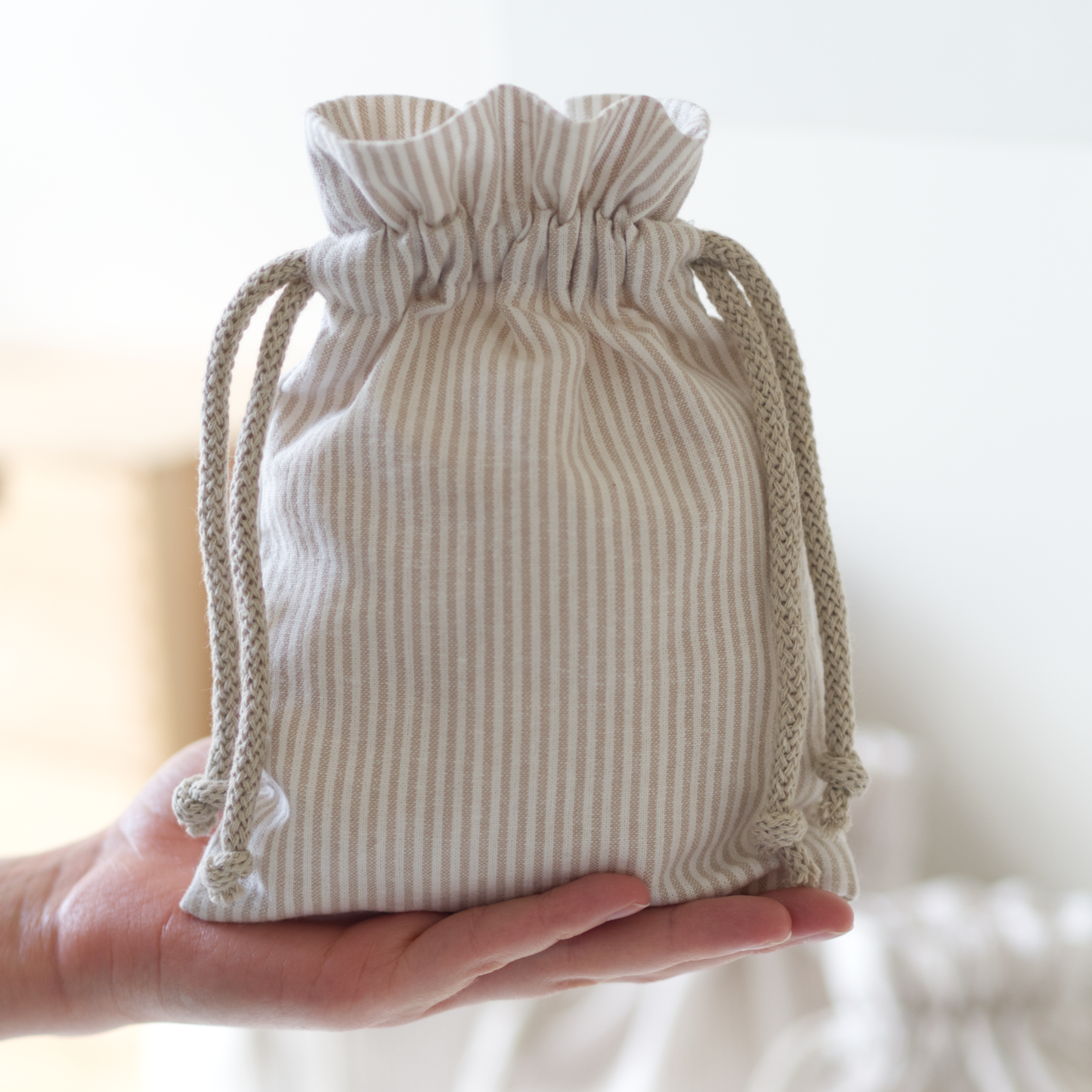 Hand holding a small striped fabric drawstring bag against a light background.