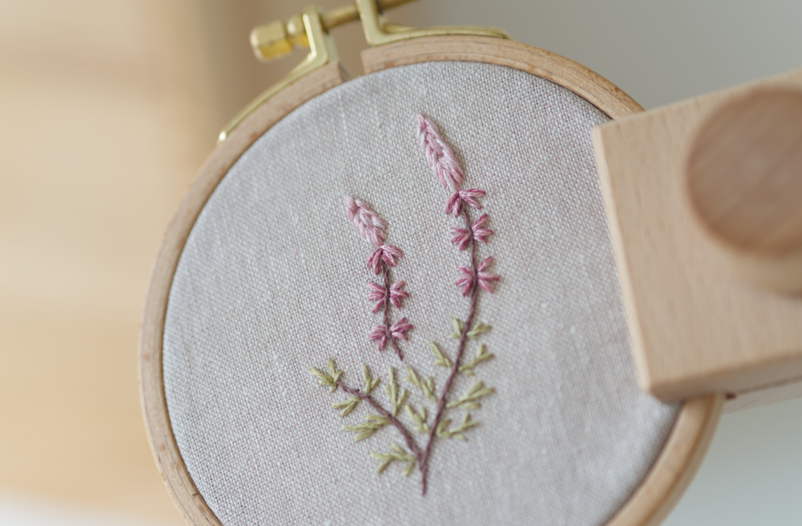 A botanical embroidery with heather design stitched in soft muted colours in an embroidery hoop.