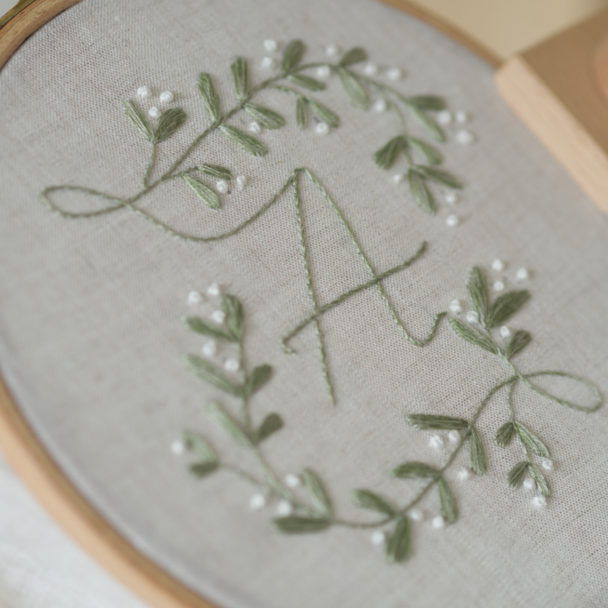 Embroidery hoop with green leaves and white flowers on grey fabric held by a person.
