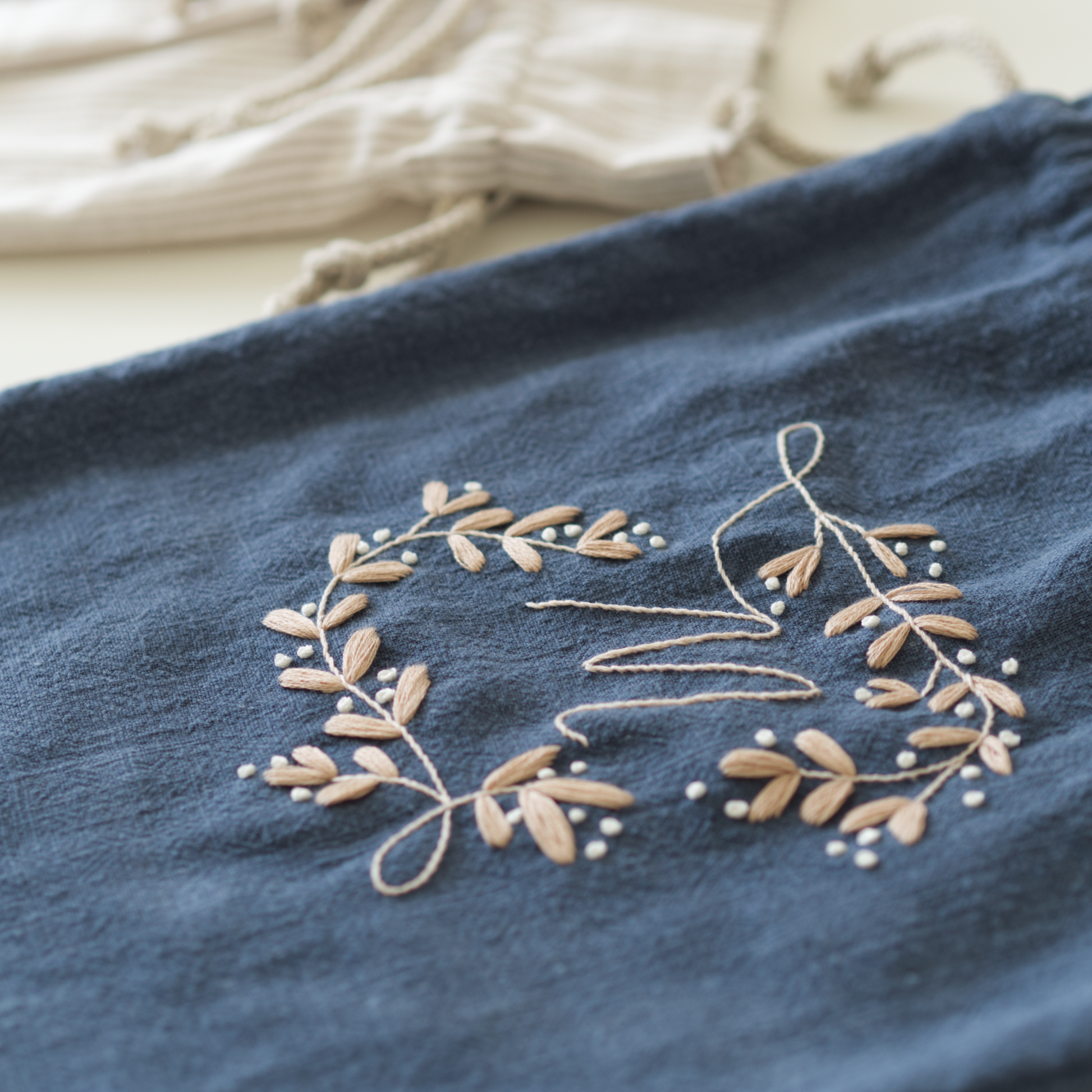 Embroidered floral design in golden thread on a blue fabric with beige background.