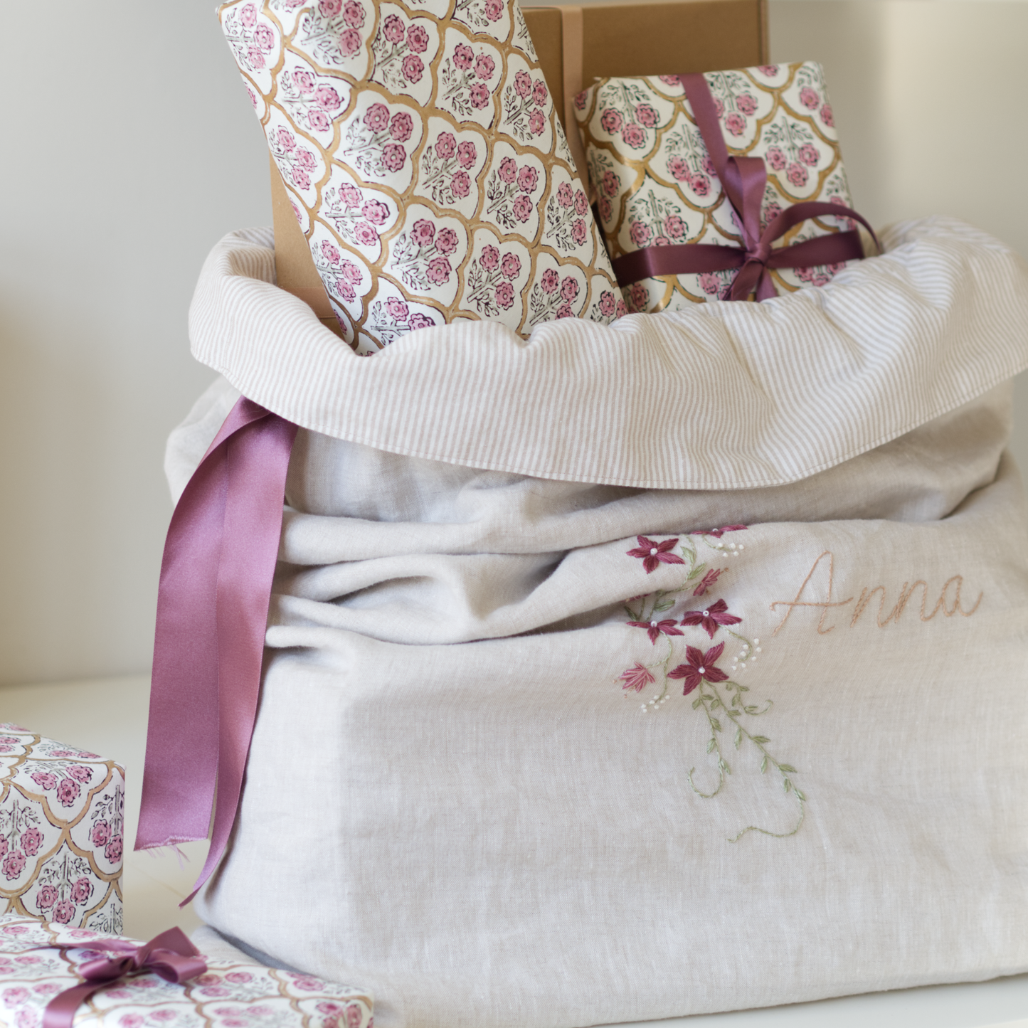 A Christmas sack in beige linen and lined with beige striped fabric filled with gifts. The sack features a botanical embroidery design with the name "Anna" and a floral vine.