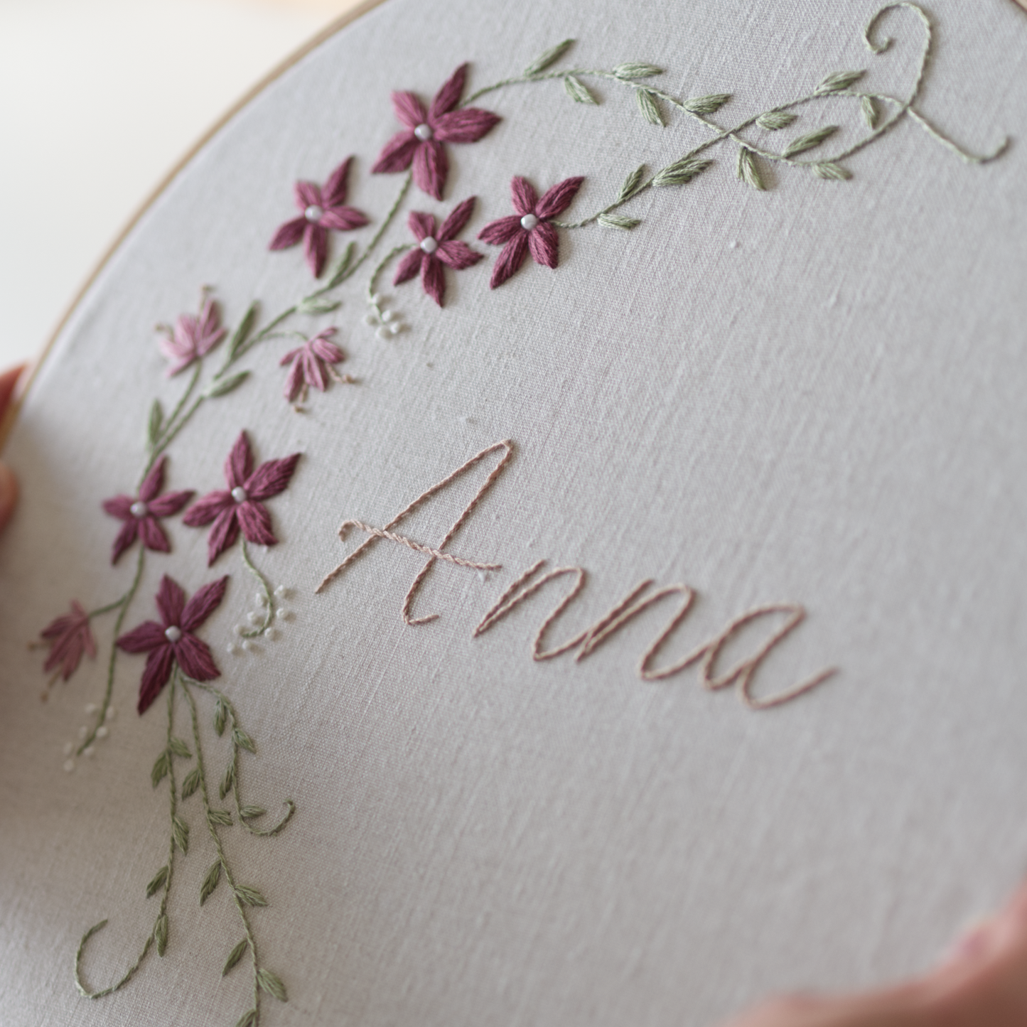 Botanical embroidery design of a winter vine in green with white berries and plum coloured flowers.