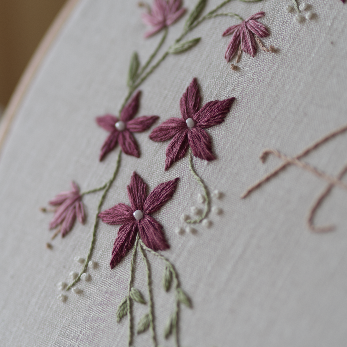 Close up of a winter vine botanical embroidery design featuring plum flowers with white bead centres, pink flowers and berry branches.