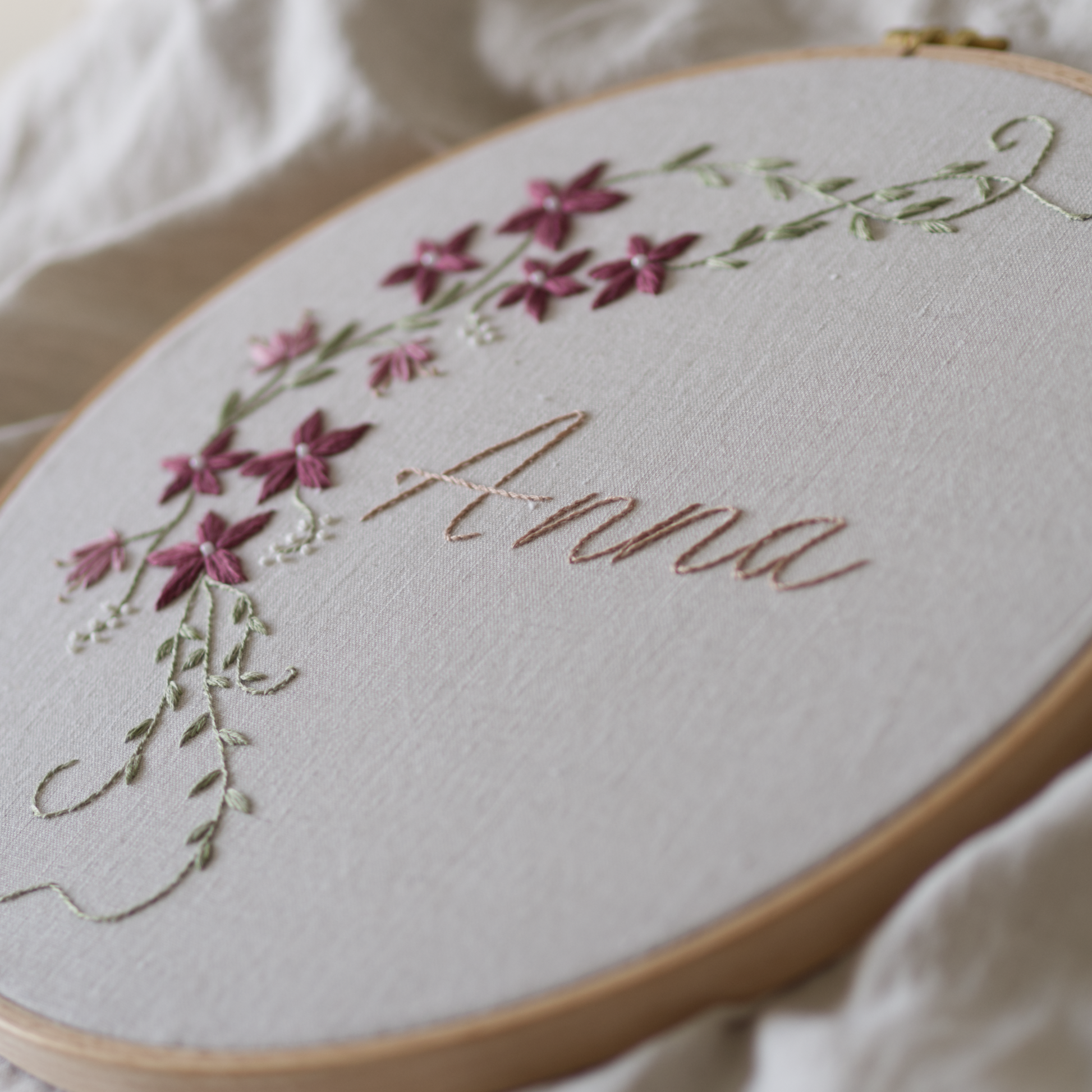 Winter vine botanical embroidery design with the name Anna in an embroidery hoop set on beige linen fabric.