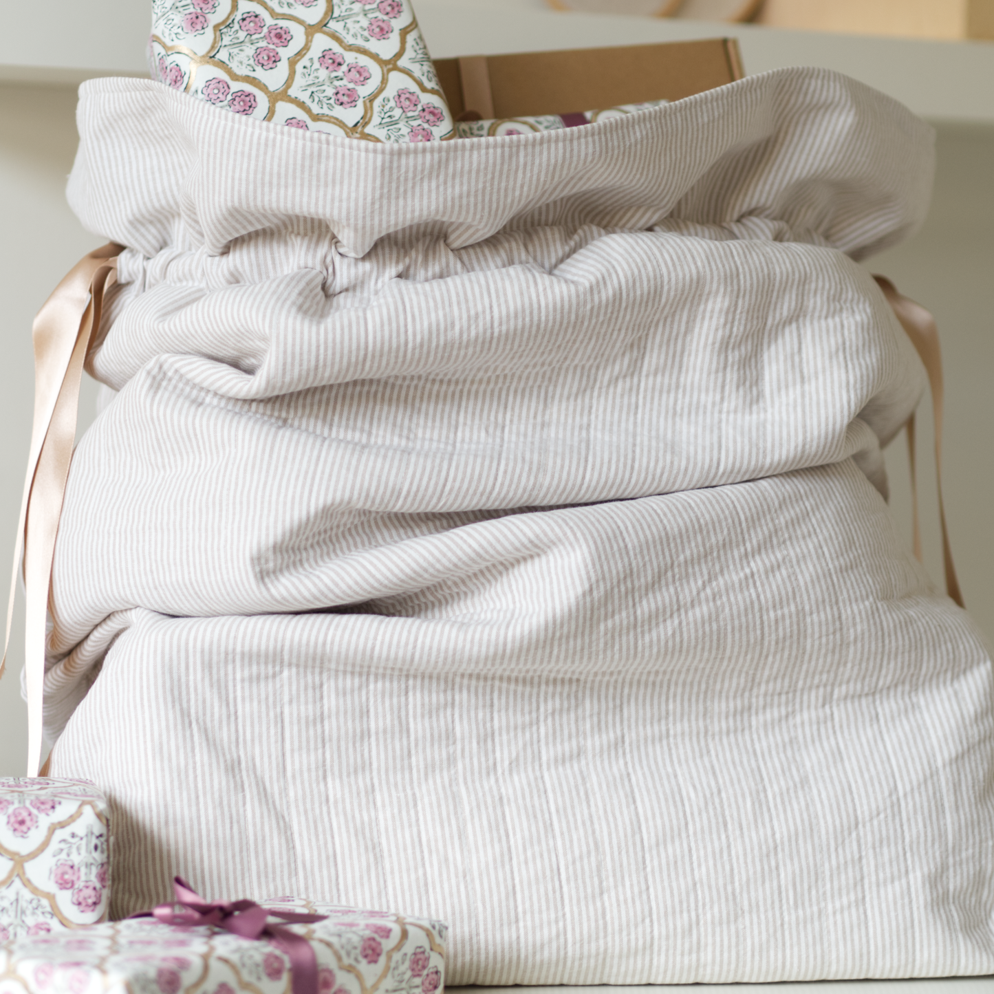 Quilted festive sack in beige striped fabric and gold ribbons holding presents.