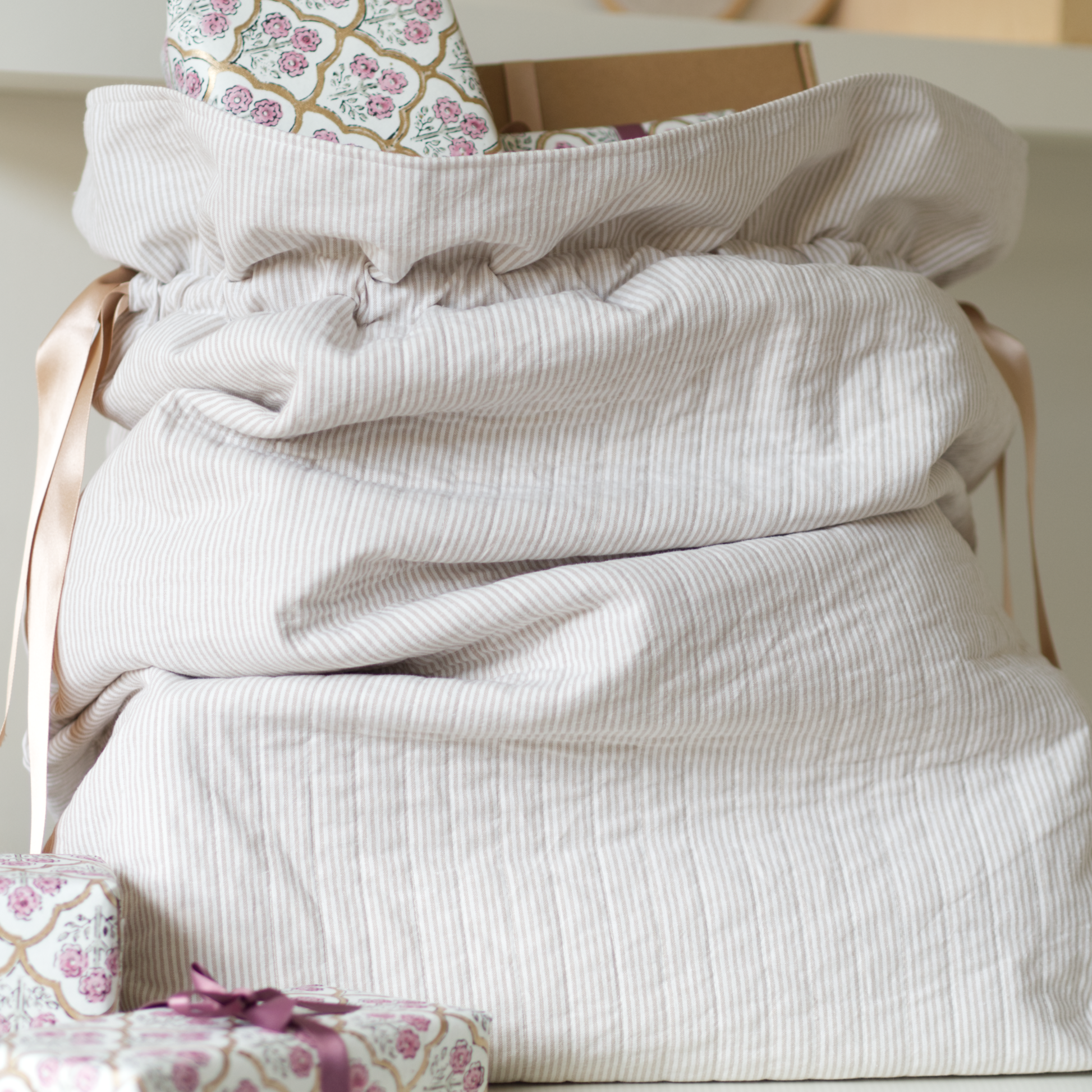 Quilted festive sack in beige striped fabric and gold ribbons holding presents.