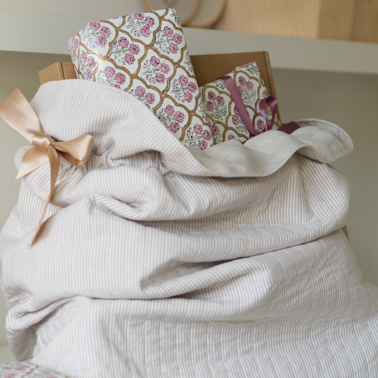 Quilted Christmas sack in beige striped fabric with gold ribbons tied in bows, filled with parcels.