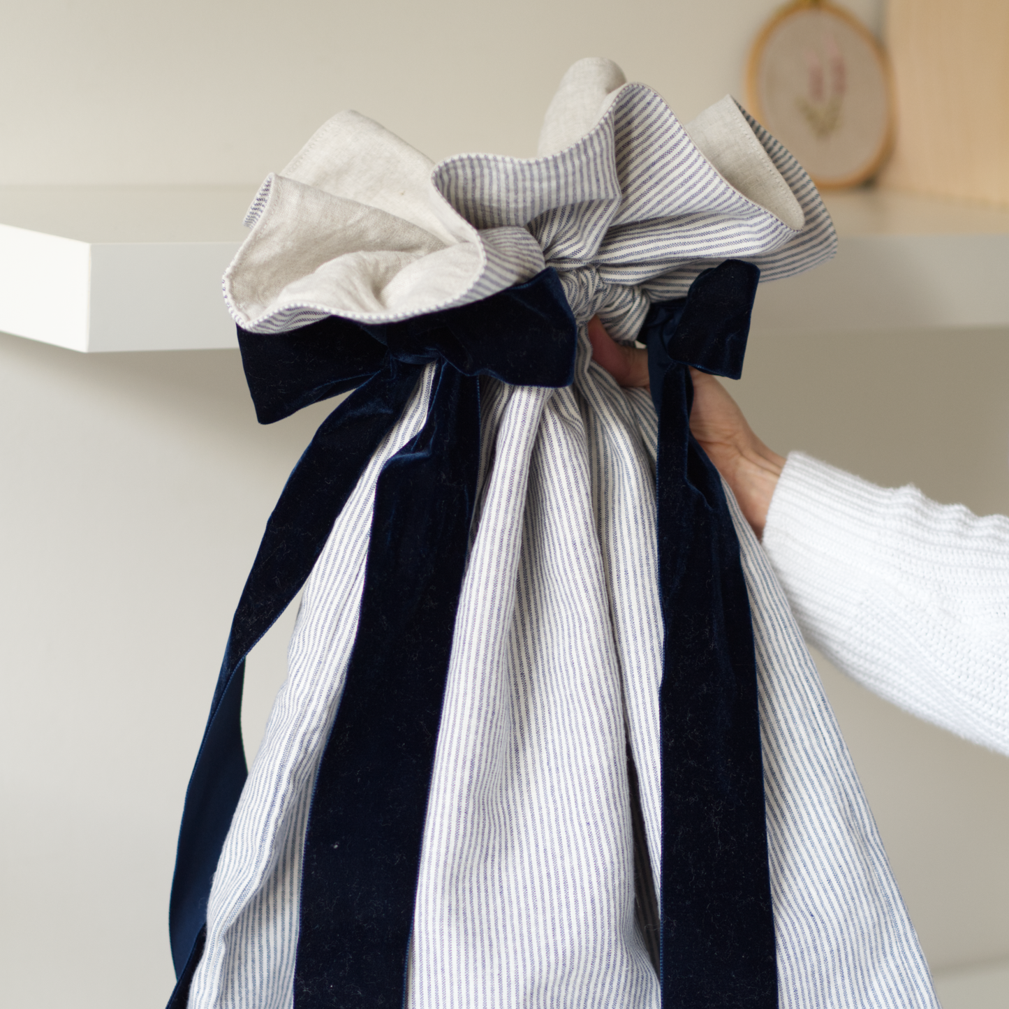 Person holding a festive sack in striped blue linen fabric with big navy velvet bows. 