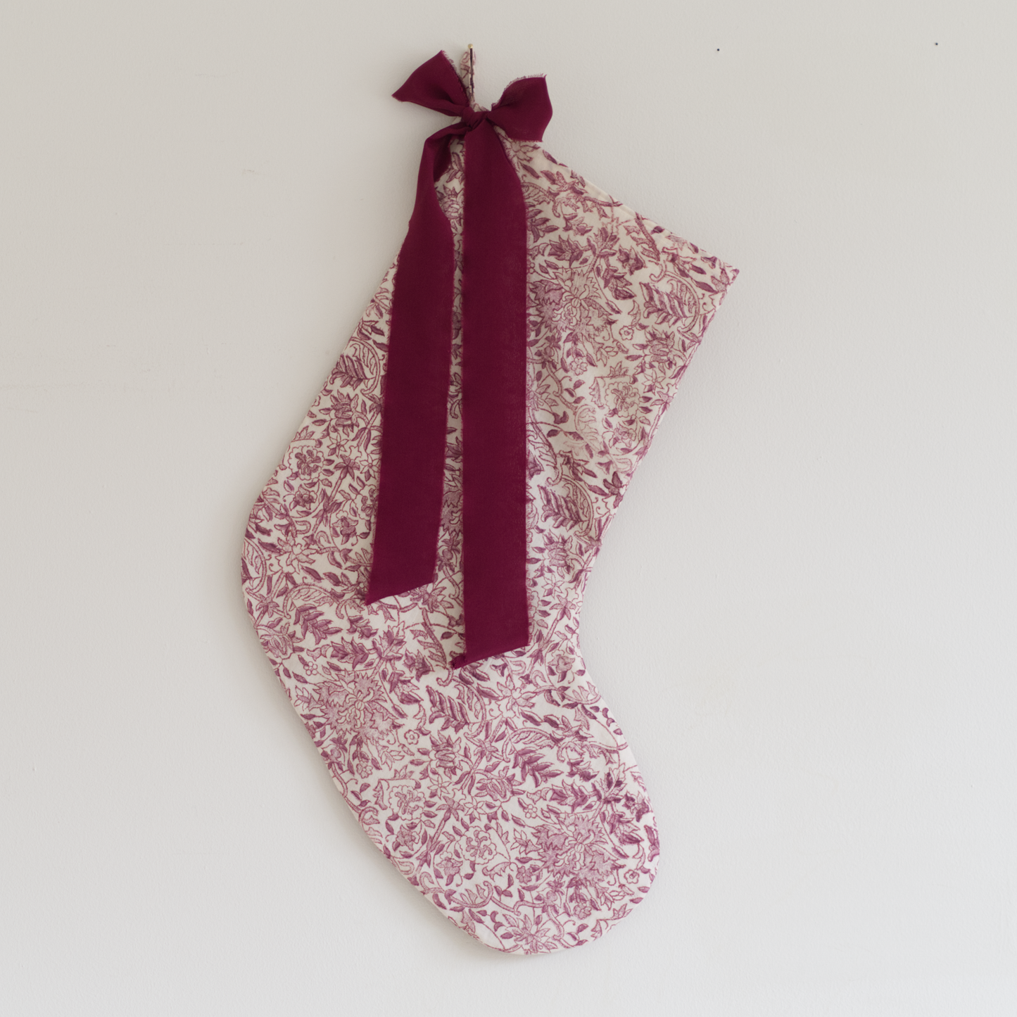 Stocking in deep pink floral fabric with a plum coloured silk ribbon tied in a bow, hung on a wall.