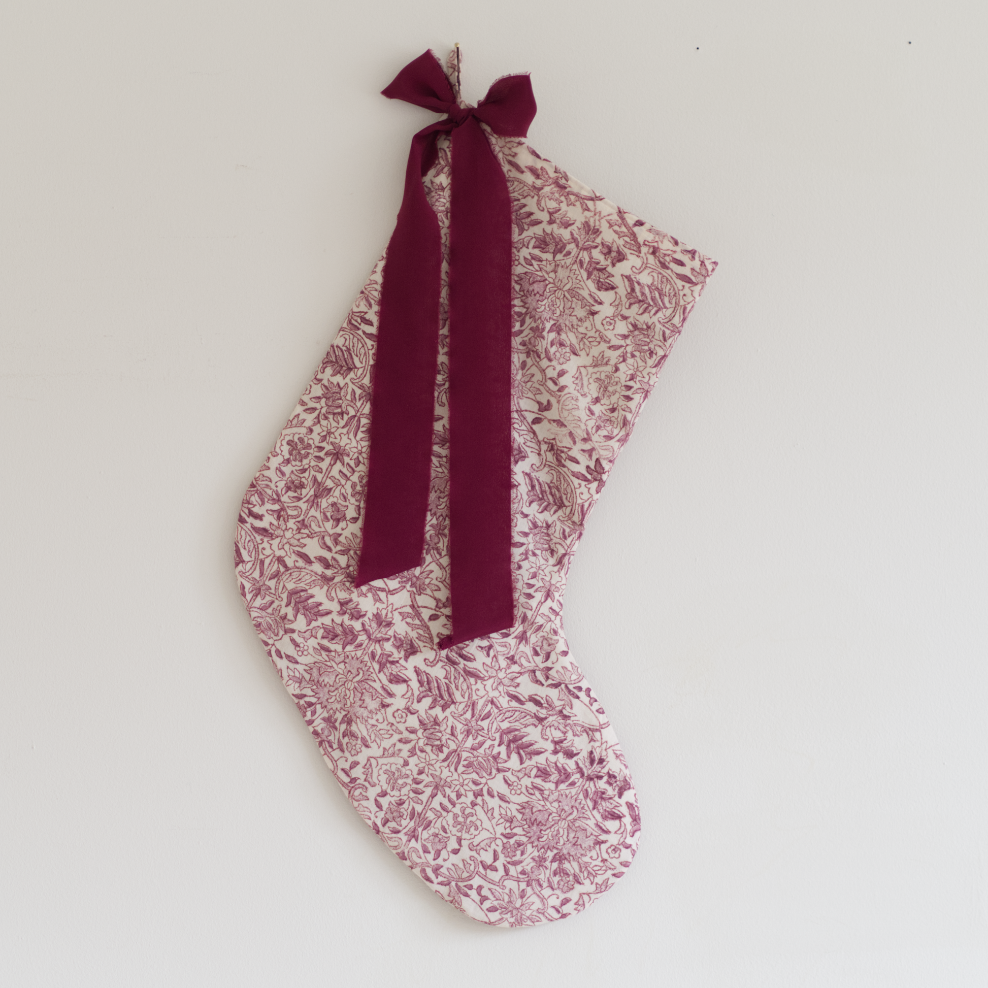 Stocking in deep pink floral fabric with a plum coloured silk ribbon tied in a bow, hung on a wall.