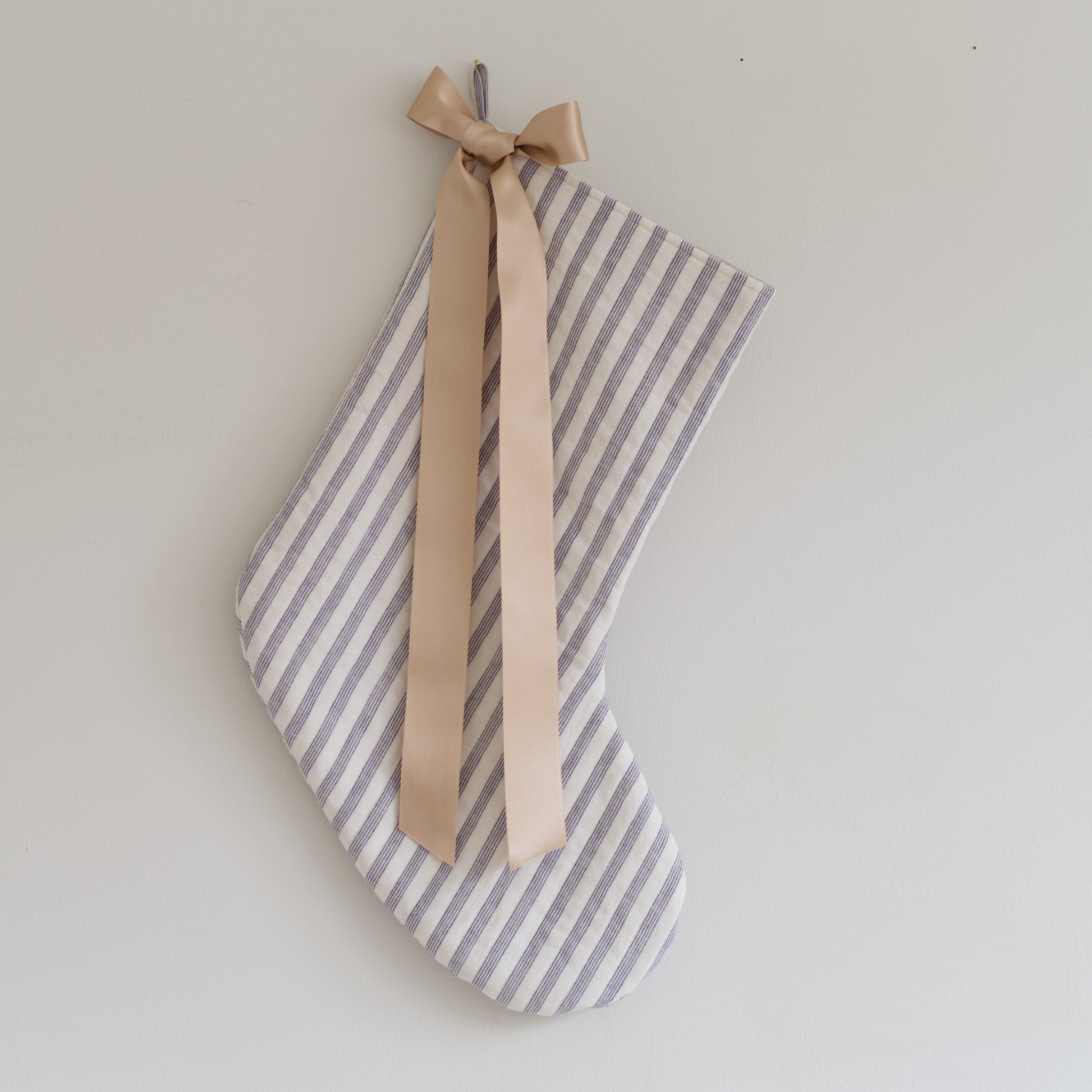 Stocking in blue striped quilted fabric with a gold ribbon tied in a bow, hung on a wall.