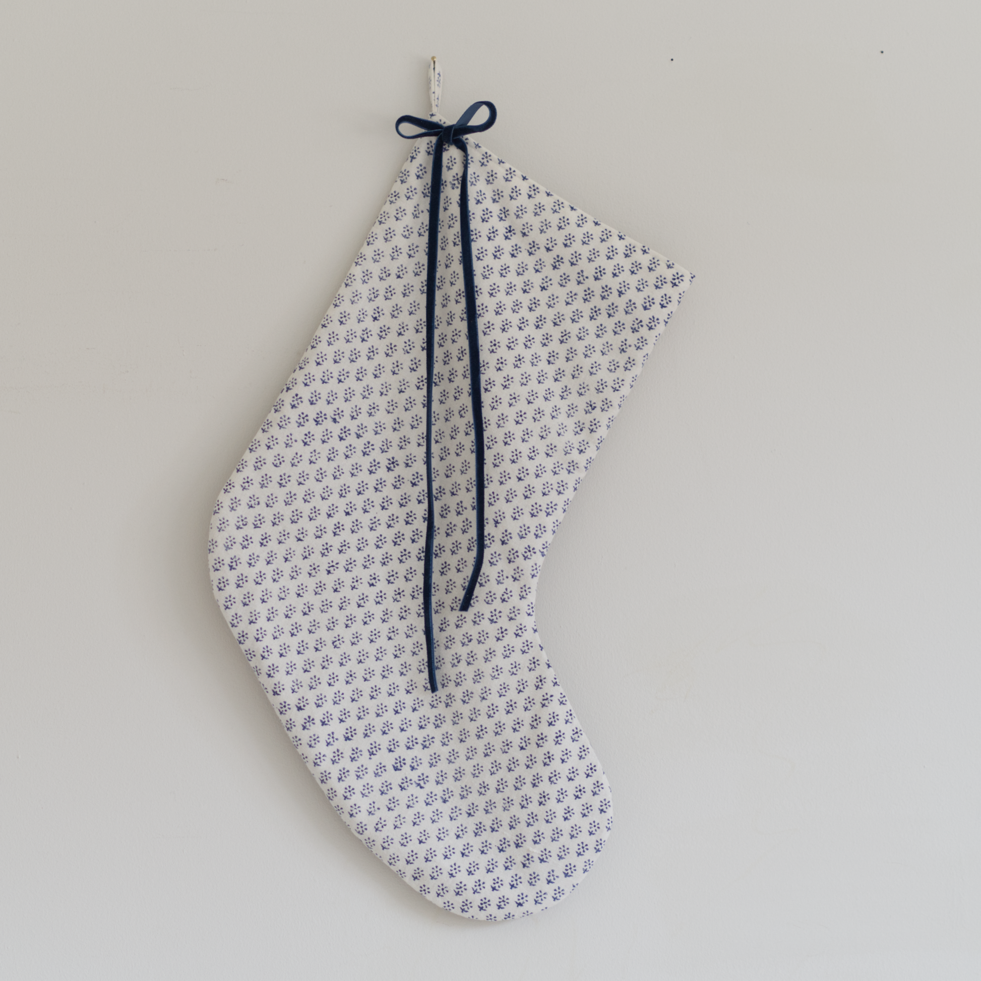 Stocking in blue block print fabric with a blue velvet ribbon tied in a bow, hung on a wall.