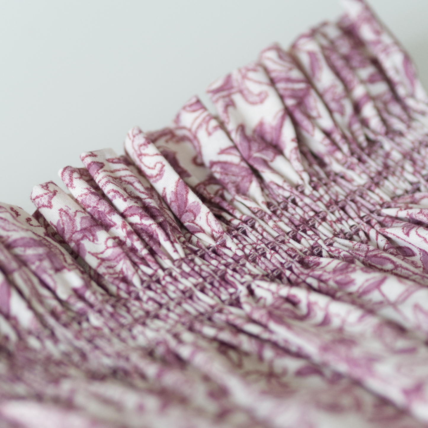Close up of a plum coloured floral fabric smocked with toho beads.