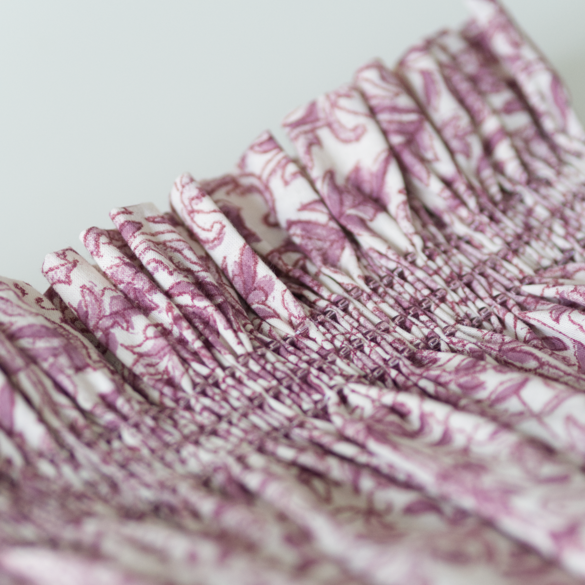 Close up of a plum coloured floral fabric smocked with toho beads.