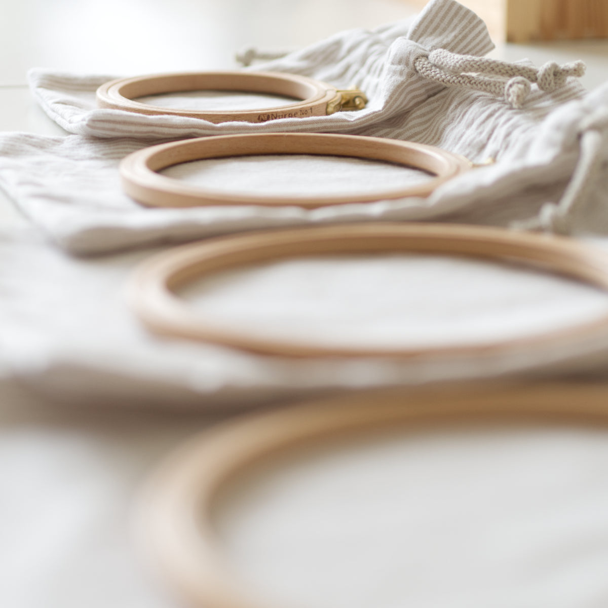 Set of four drawstring bags in different sizes laid out flat with a corresponding embroidery hoop on top of each, ready to embroider.