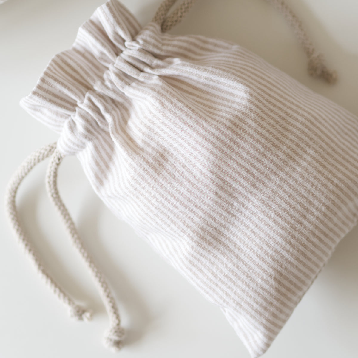 Close up of a small drawstring bag in beige striped fabric.
