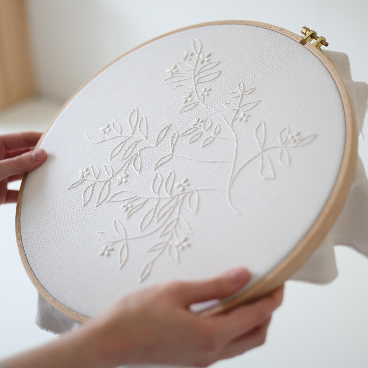 Side view of The Branch botanical embroidery stitched in cream thread in a wooden hoop